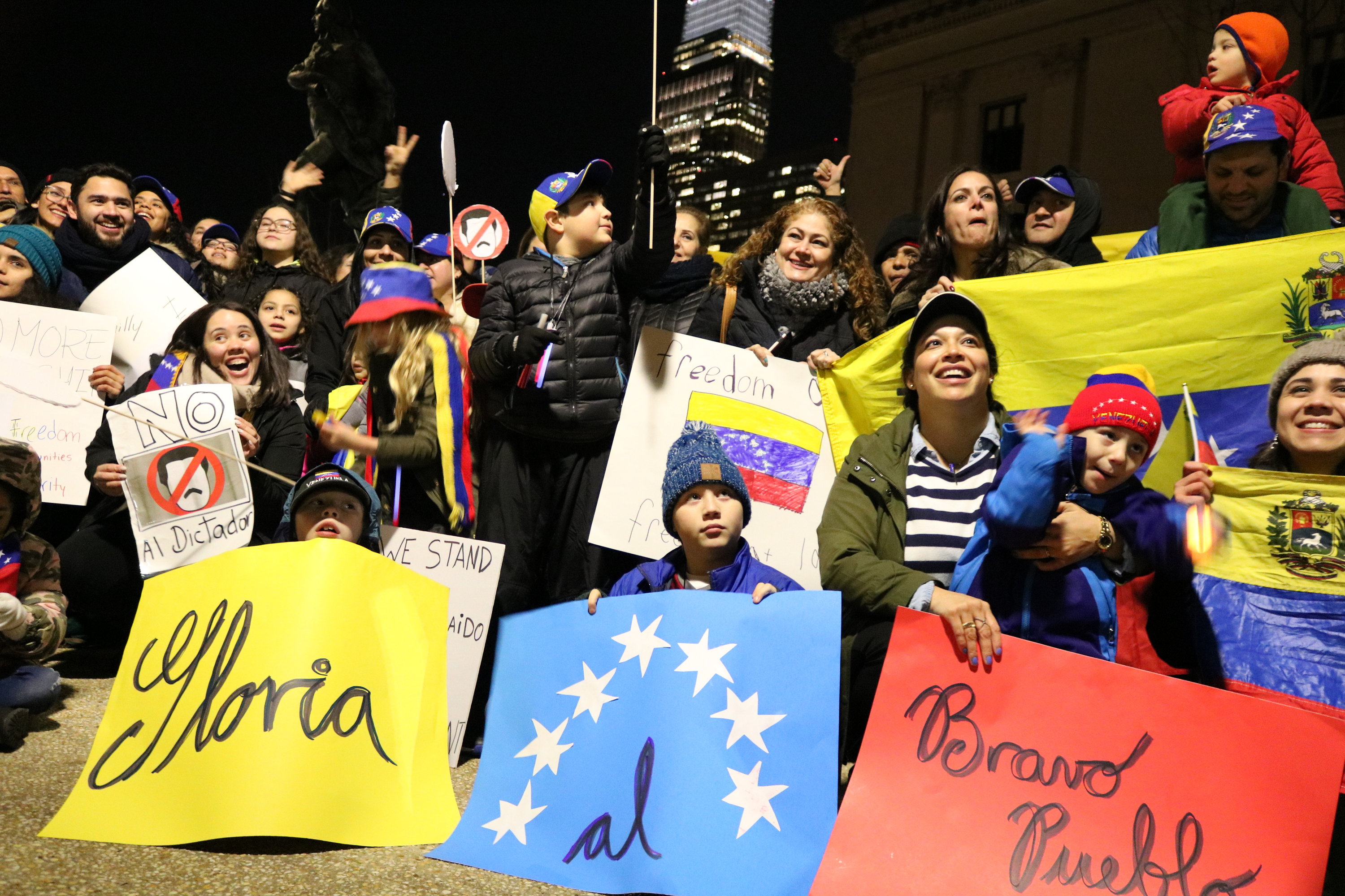 Rosana Arteaga-Lopenza (center-right) and her three sons, Henry, Miguelangelo and Simón, hold signs with lyrics of the Venezuelan national athem: Gloria al Bravo Pueblo. Photo: Greta Anderson / AL DÍA News