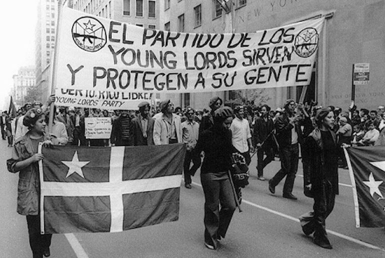 Young Lords members march with a sign that reads, "The Party of the Young Lords serves and protects your people." Iris Morales. ¡Palante, Siempre Palante!, 1996. Film.