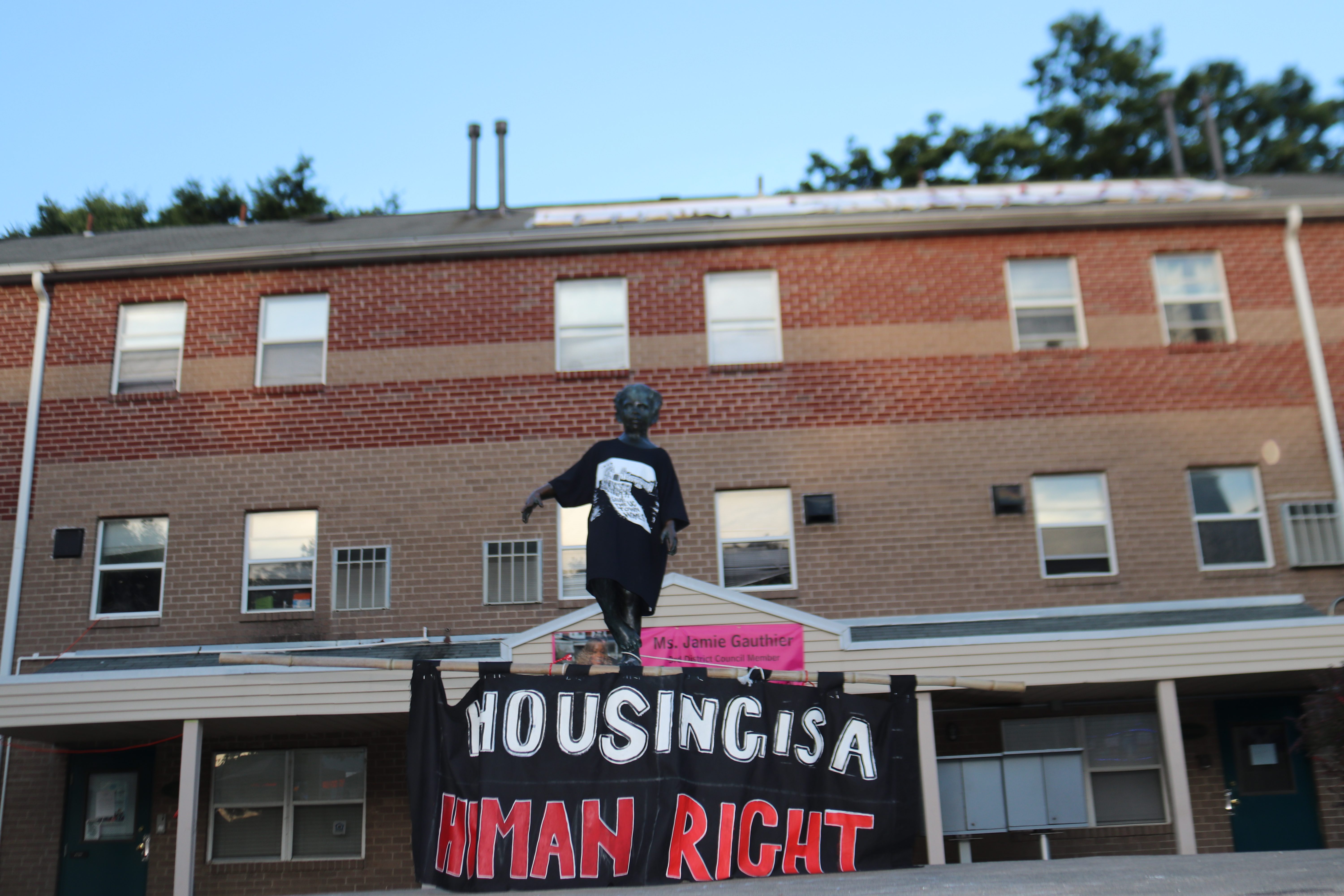 Pictured: Statue of female child in courtyard, wearing garment tat reads Housing is a Human Right