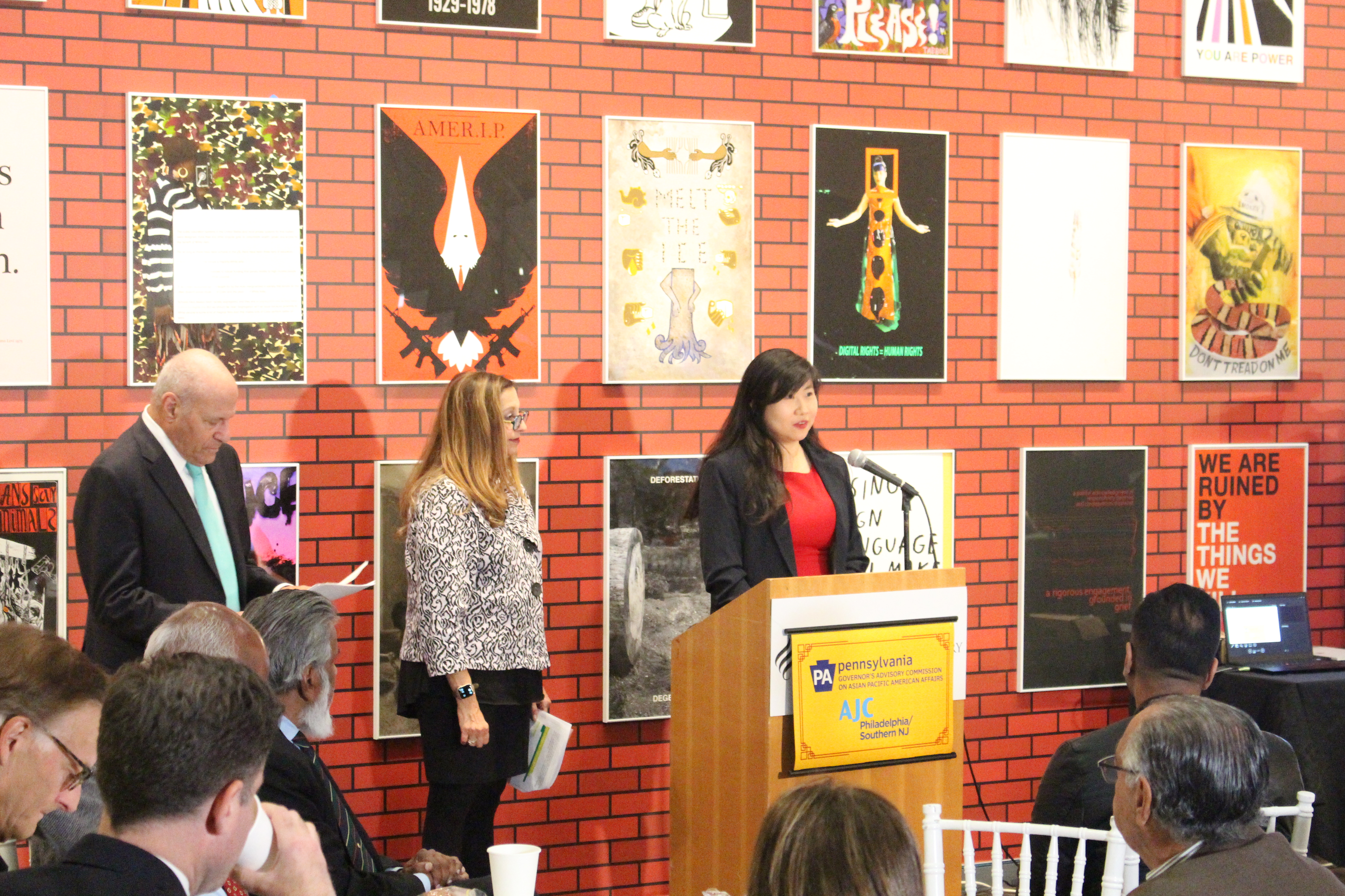 Stephanie Sun speaks at a podium besides Alan Hoffman and Marcia Bronstein