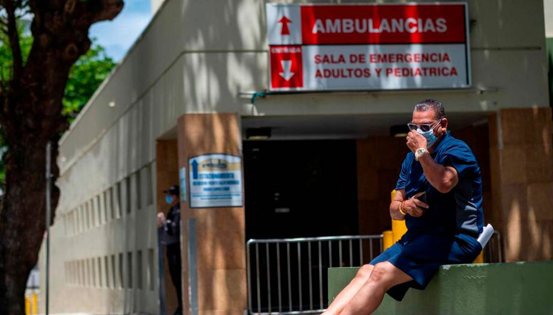 Un hombre con una máscara quirúrgica se sienta frente a la entrada de la sala de emergencias del Hospital Comunitario Presbiteriano de Ashford en San Juan, Puerto Rico, donde el primer paciente con coronavirus de la isla murió ese mismo día, el 21 de marz