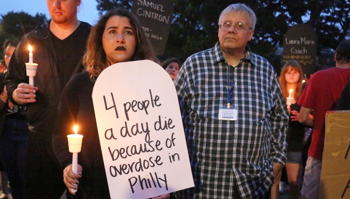 A woman holds a candle during the vigil at McPherson Square. Her signs read “4 people a day die because of an overdose in Philly.”